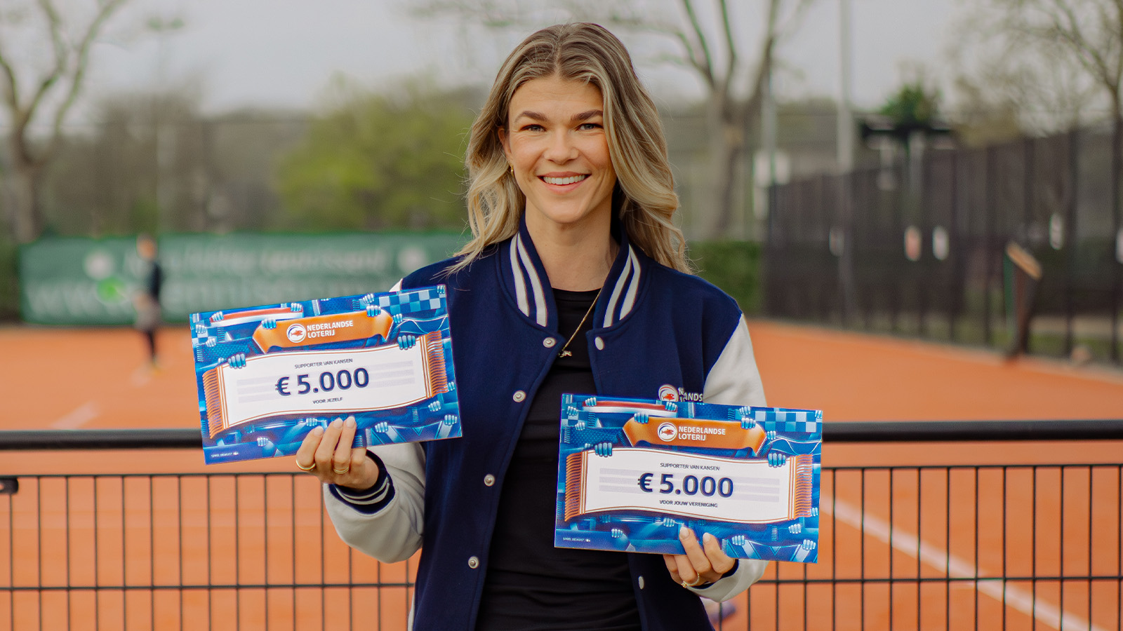 Tess Lieder toont twee cheques van € 5.000 op een tennisbaan.